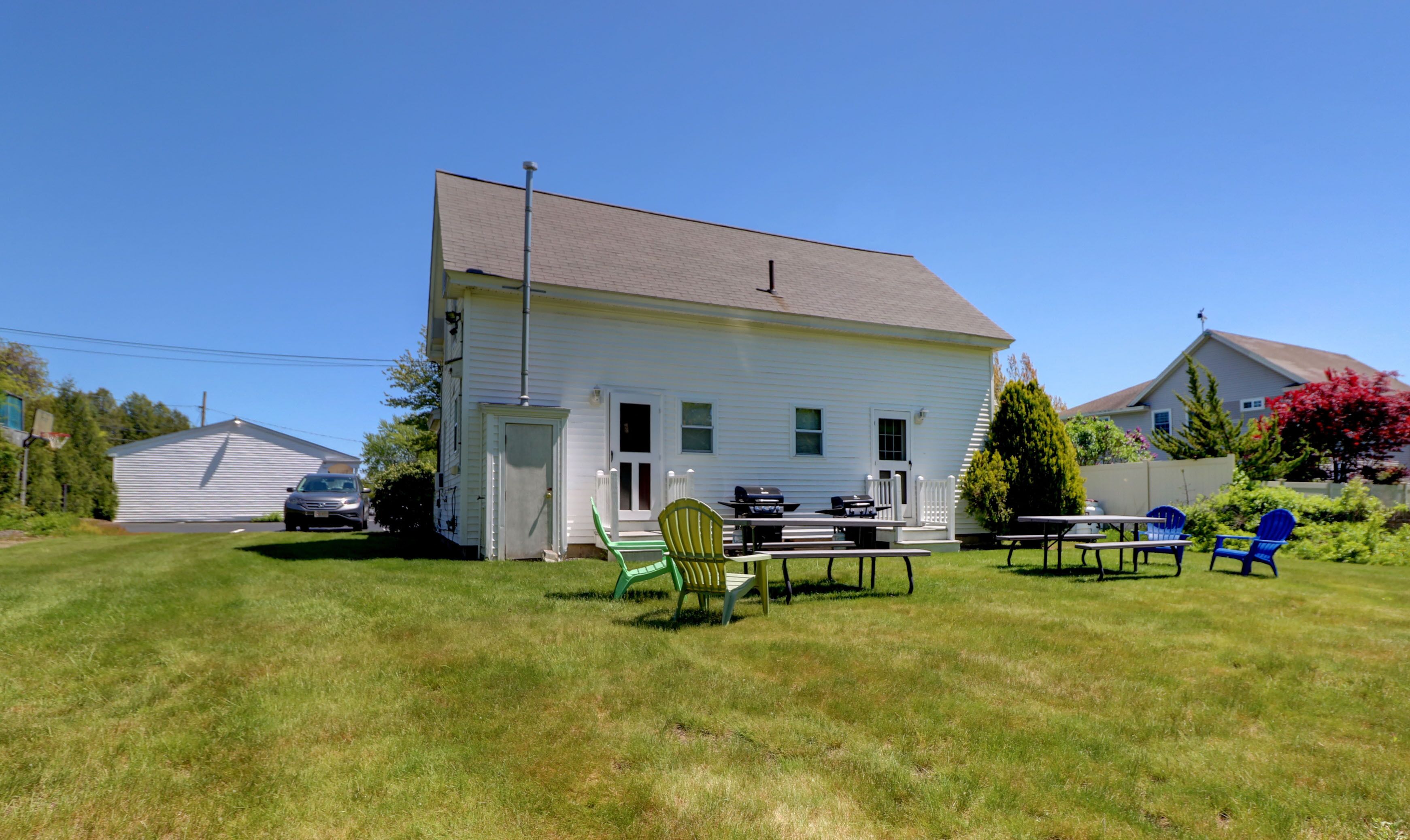 A white house with a front porch, a lawn, and outdoor furniture.