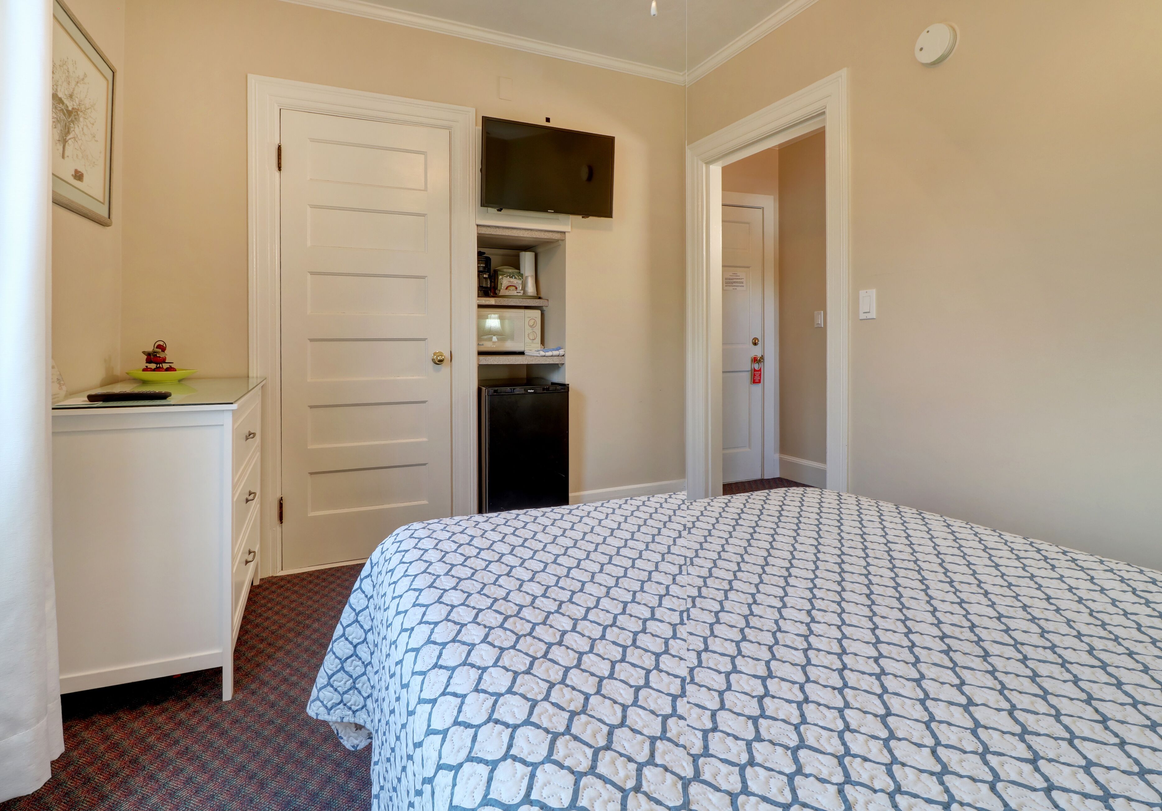 A bedroom with a bed, a dresser, a microwave, and a television mounted above the dresser.