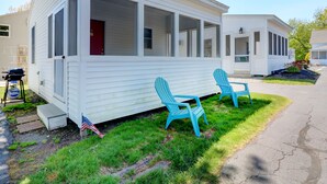 A white mobile home with a porch, two blue Adirondack chairs, and an American flag on the front step. - Carriage House Motel Cottages & Suites (Wells)