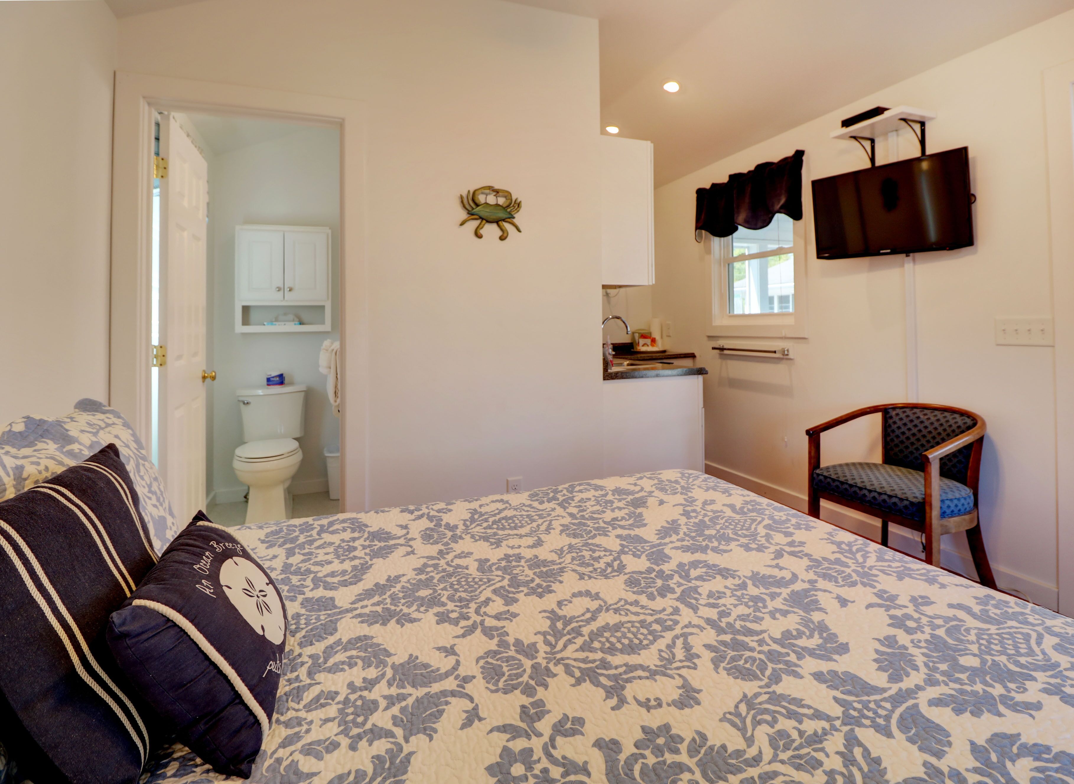 A bedroom with a bed, a chair, a television, and a bathroom visible through an open door.