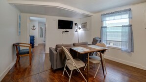 A living room with a sofa, a dining table with chairs, a TV mounted on the wall, and a window with curtains. - Carriage House Motel Cottages & Suites (Wells)