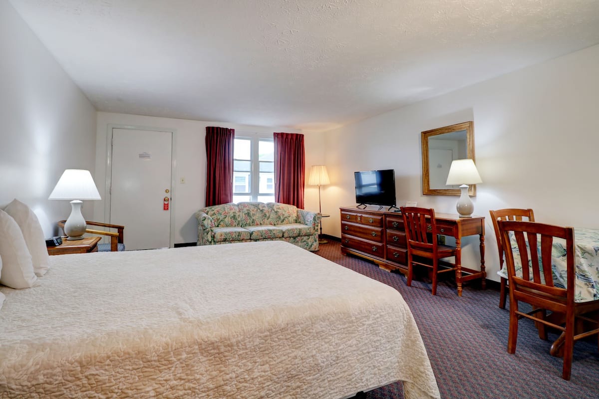 Een hotelkamer met een groot bed, een bloemenbank, een houten bureau met een televisie en een spiegel aan de muur.