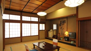 Ett traditionellt japanskt rum med tatamimattor på golvet, ett lågt bord, en tv och en dekorativ lampa.