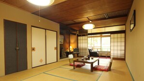 Ett traditionellt japanskt rum med tatamimattor på golvet, skjutdörrar, ett lågt bord med kuddar och en tv.