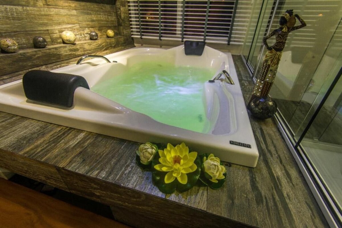 Una bañera de hidromasaje con encimera de madera, una estatua y flores decorativas.