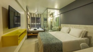 Een moderne hotelkamer met een groot bed, een klein zithoekje, een badkamer met glazen wanden en een flatscreen televisie aan de muur.