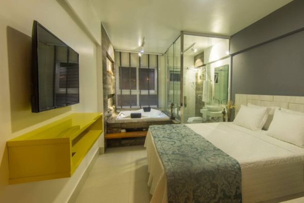 Una habitación de hotel moderna con una cama grande, una pequeña zona de estar, un baño con paredes de vidrio y un televisor de pantalla plana montado en la pared.