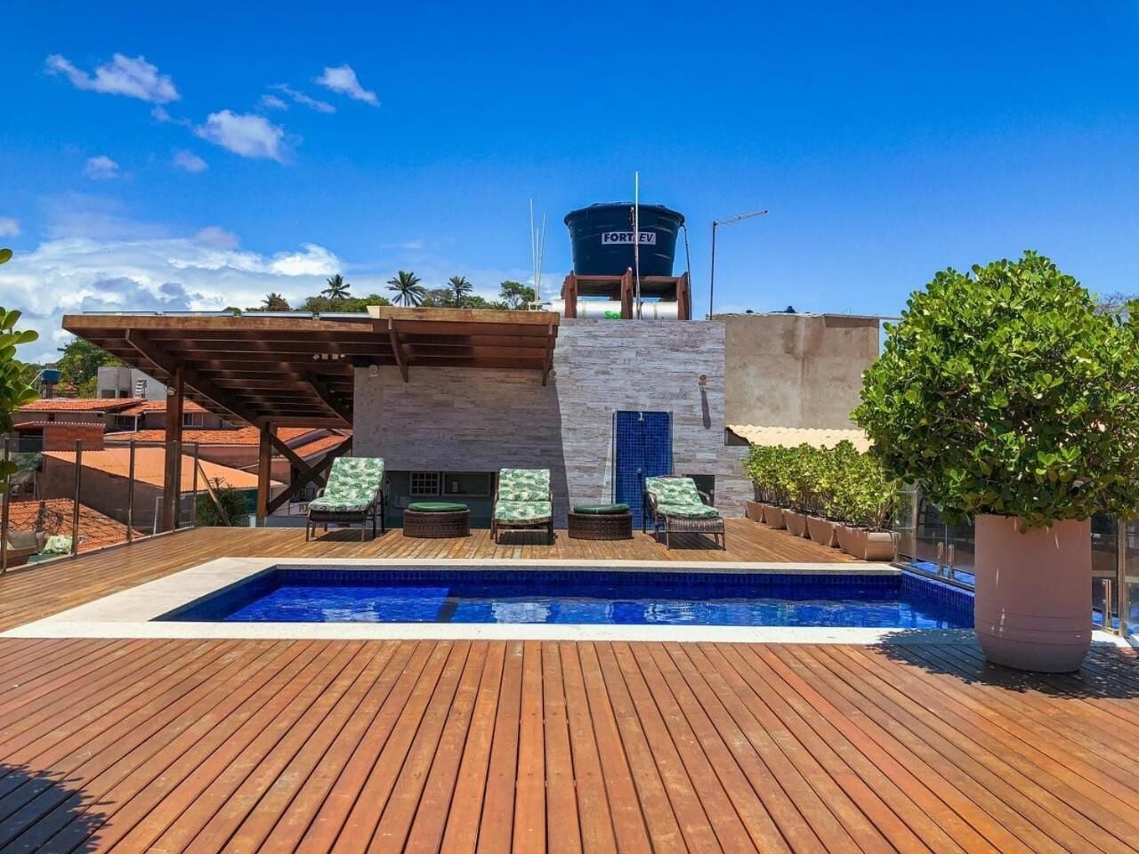 A rooftop pool area with a wooden deck, lounge chairs, and a water tank labeled "FORT EV".