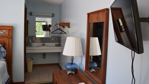 A bathroom with a wooden vanity, a mirror, a blue lamp, and a television mounted on the wall.