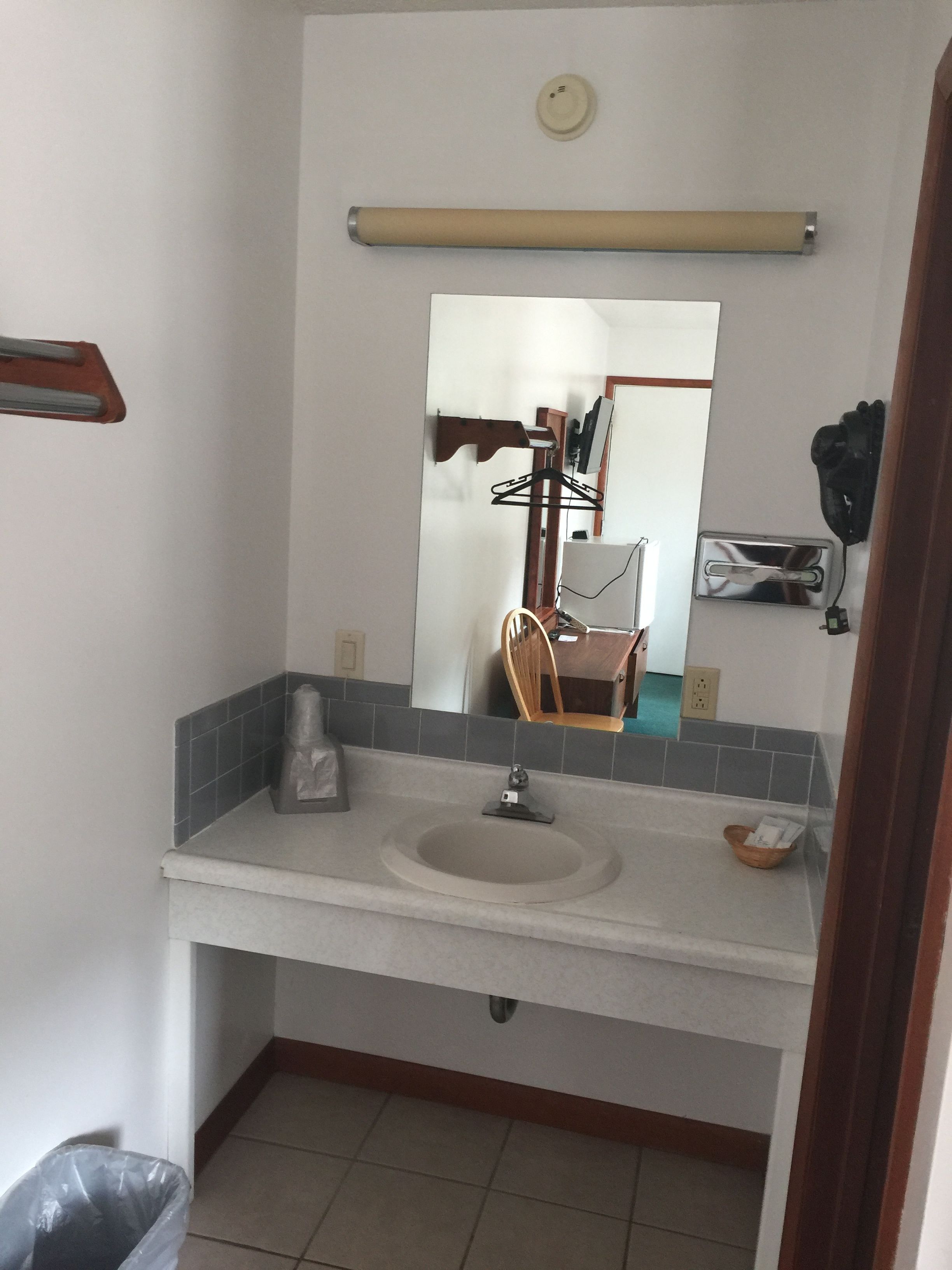 Un baño con lavamanos, espejo, toallero y un pequeño cubo de basura.