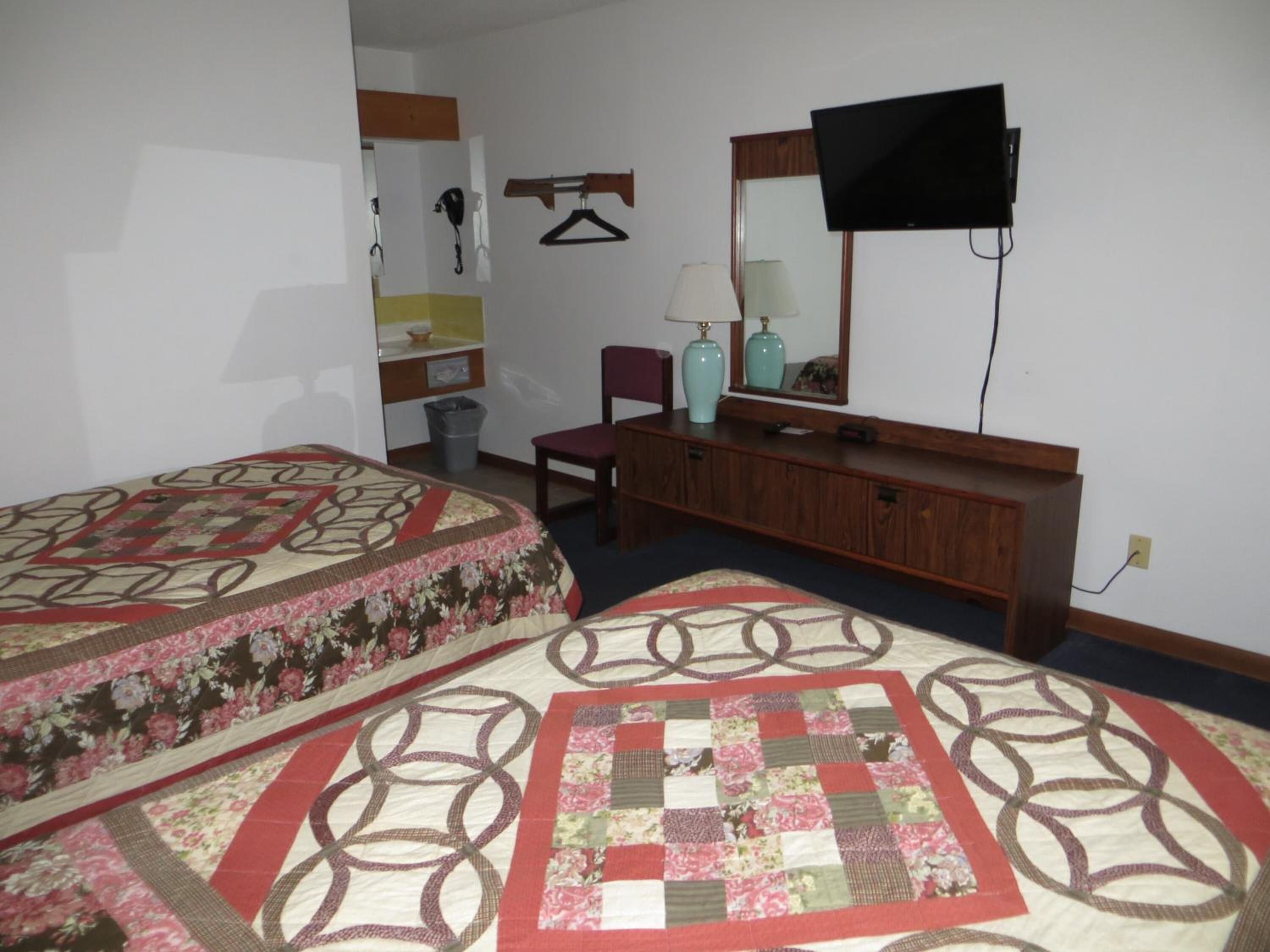 A bedroom with two beds, a dresser, a television, and a mirror.