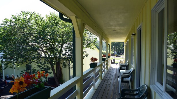 A covered outdoor seating area with wooden benches and tables, surrounded by yellow walls and windows.