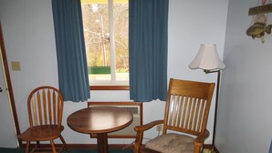 A room with a wooden table and two chairs, a lamp, and a window with curtains.