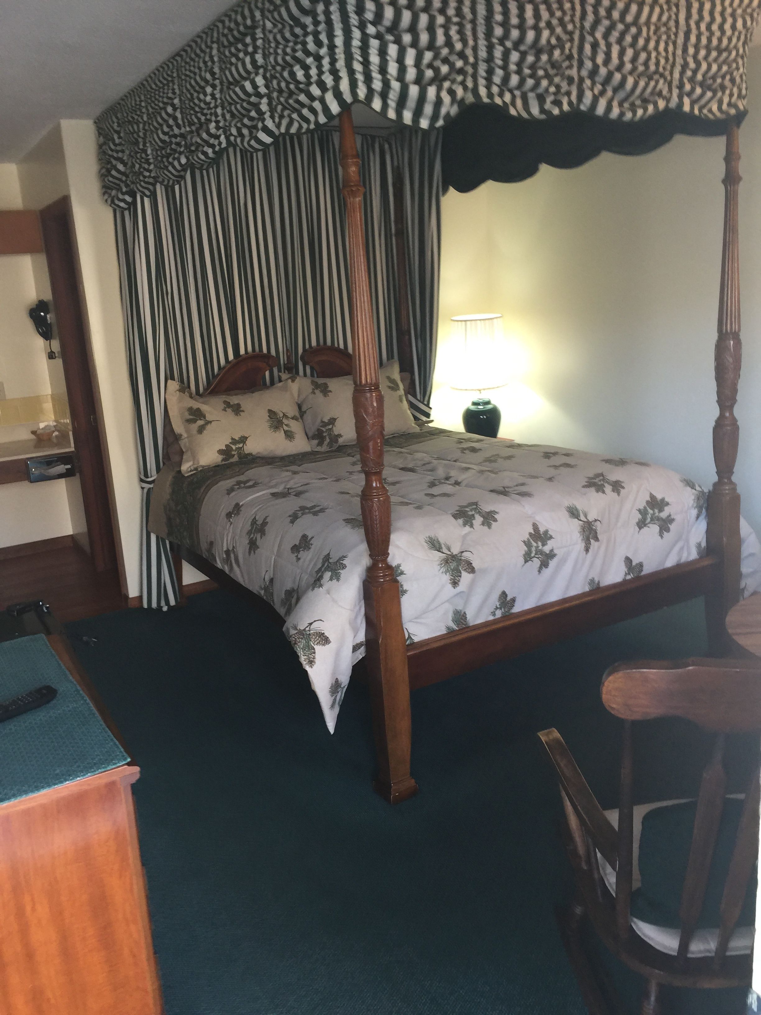 A four-poster canopy bed with a floral bedspread, a wooden nightstand, and a chair.
