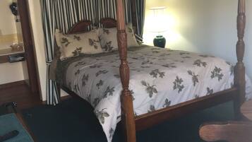 A four-poster canopy bed with a floral bedspread, a wooden nightstand, and a chair.