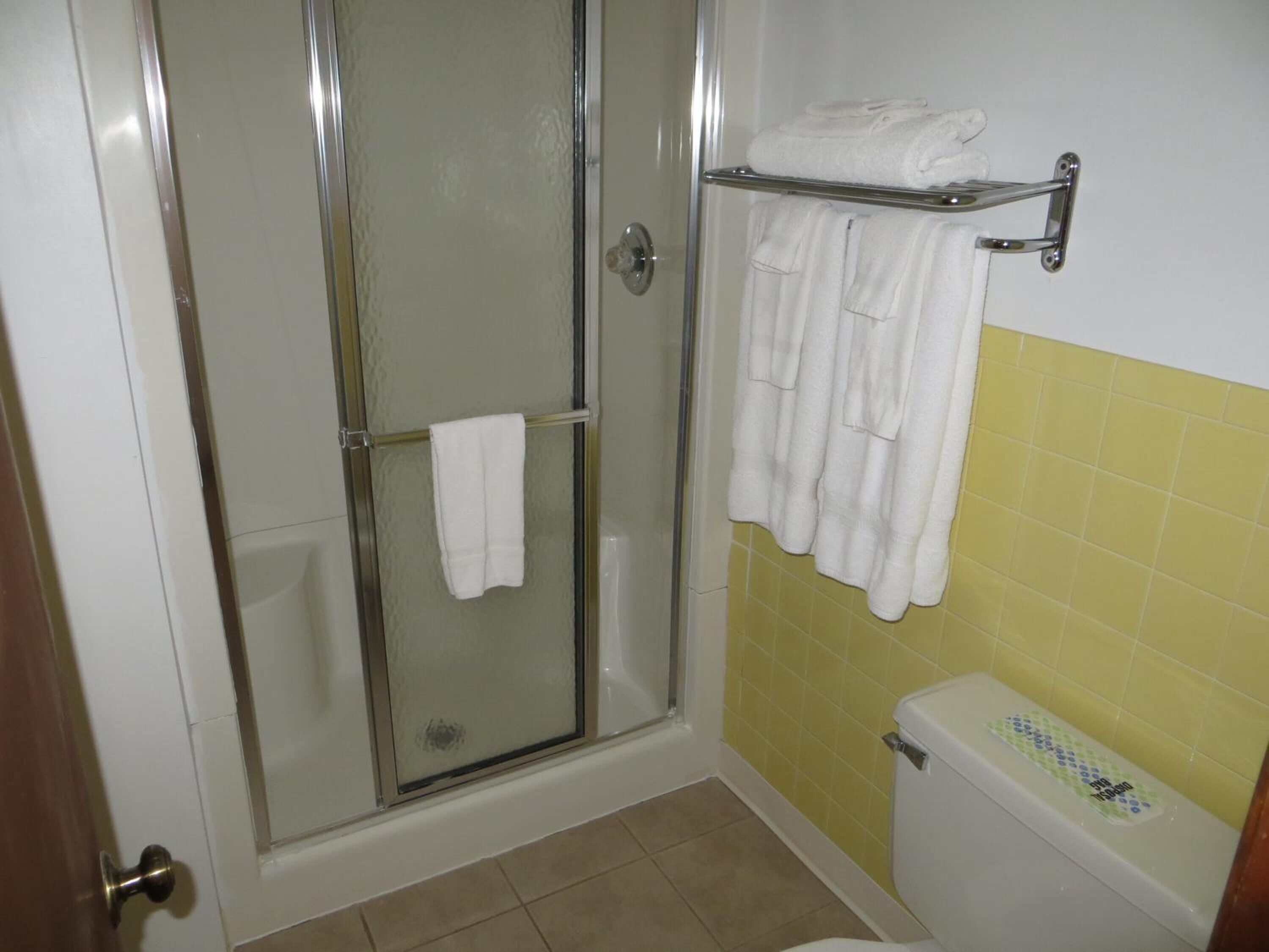 Een badkamer met een douchecabine van glas, een wit toilet en een gele betegelde muur.