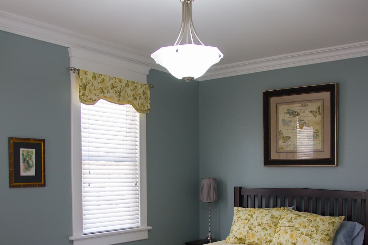 A bedroom with a bed, a window with blinds, a bedside lamp, and a framed picture on the wall.