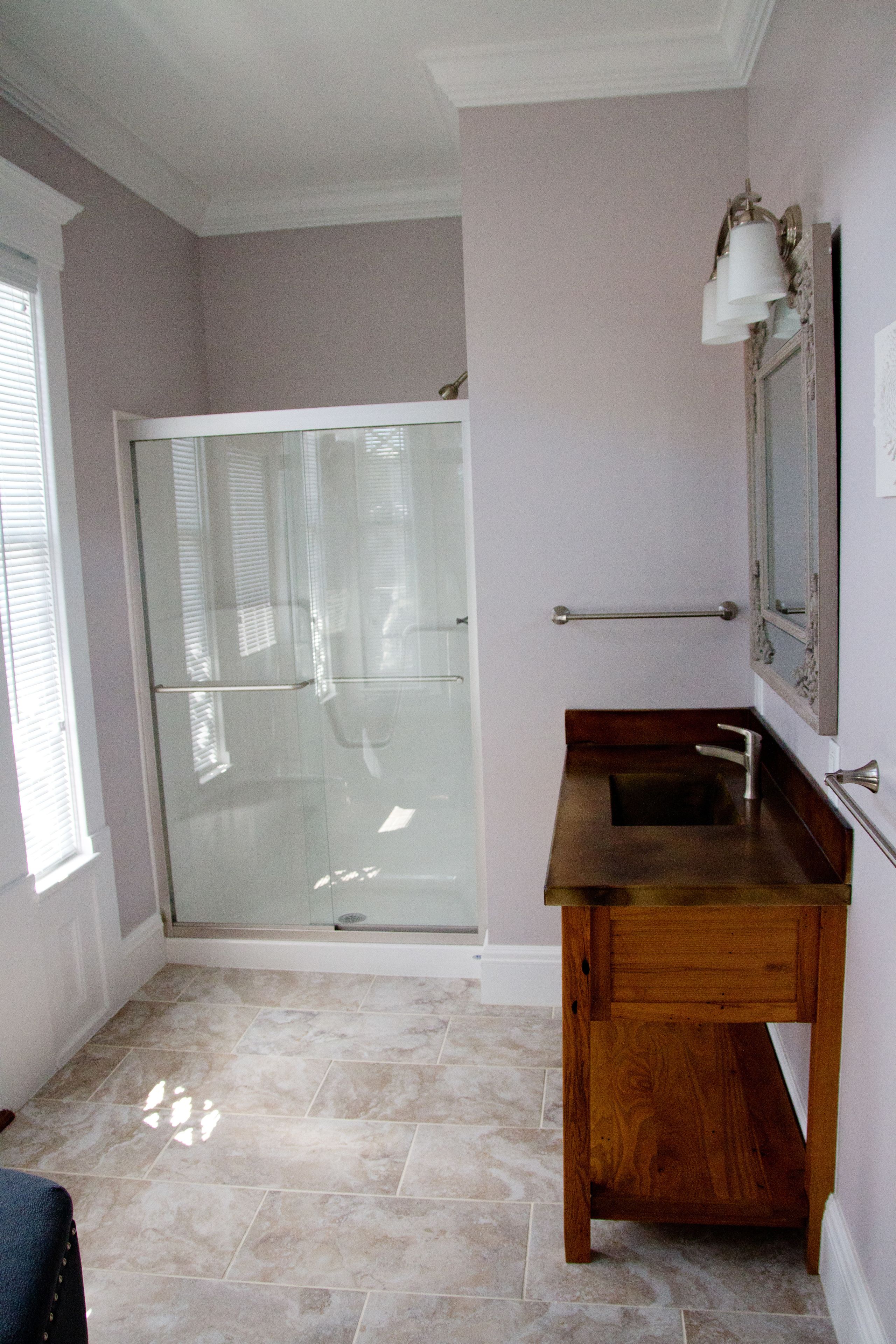 Une salle de bain avec une porte de douche en verre, un meuble-lavabo en bois et un miroir avec un luminaire intégré.