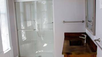 Une salle de bain avec une porte de douche en verre, un meuble-lavabo en bois et un miroir avec un luminaire intégré.