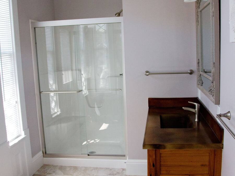 Une salle de bain avec une porte de douche en verre, un meuble-lavabo en bois et un miroir avec un luminaire intégré.