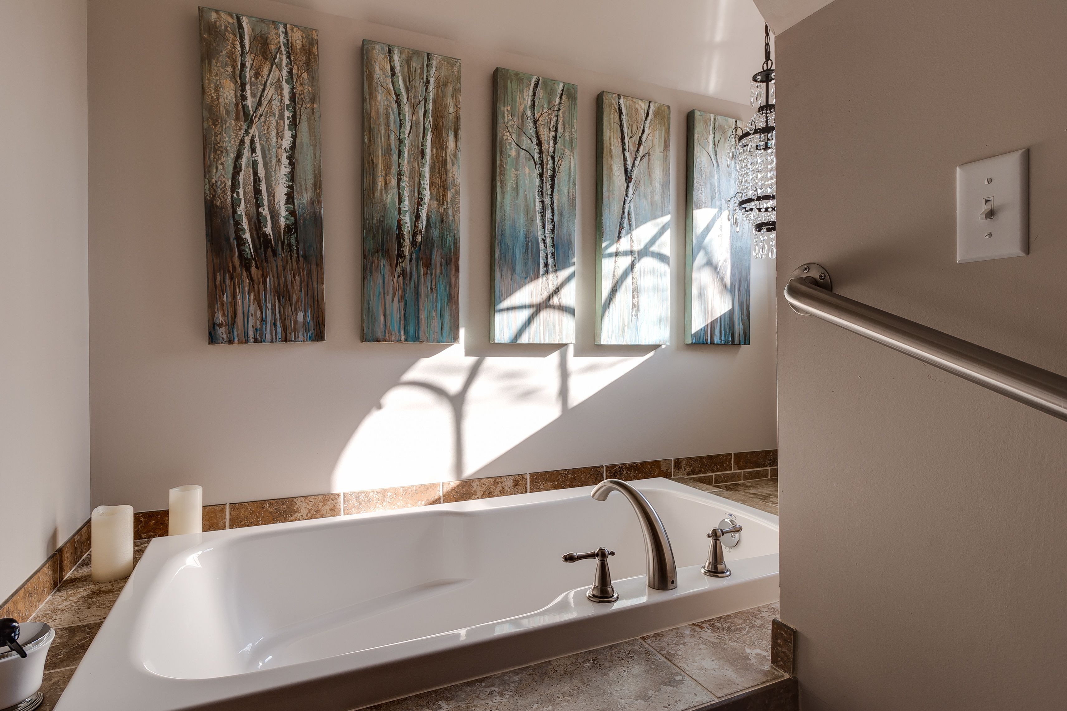 A modern bathroom with a freestanding bathtub, a handrail, and a series of abstract paintings on the wall.