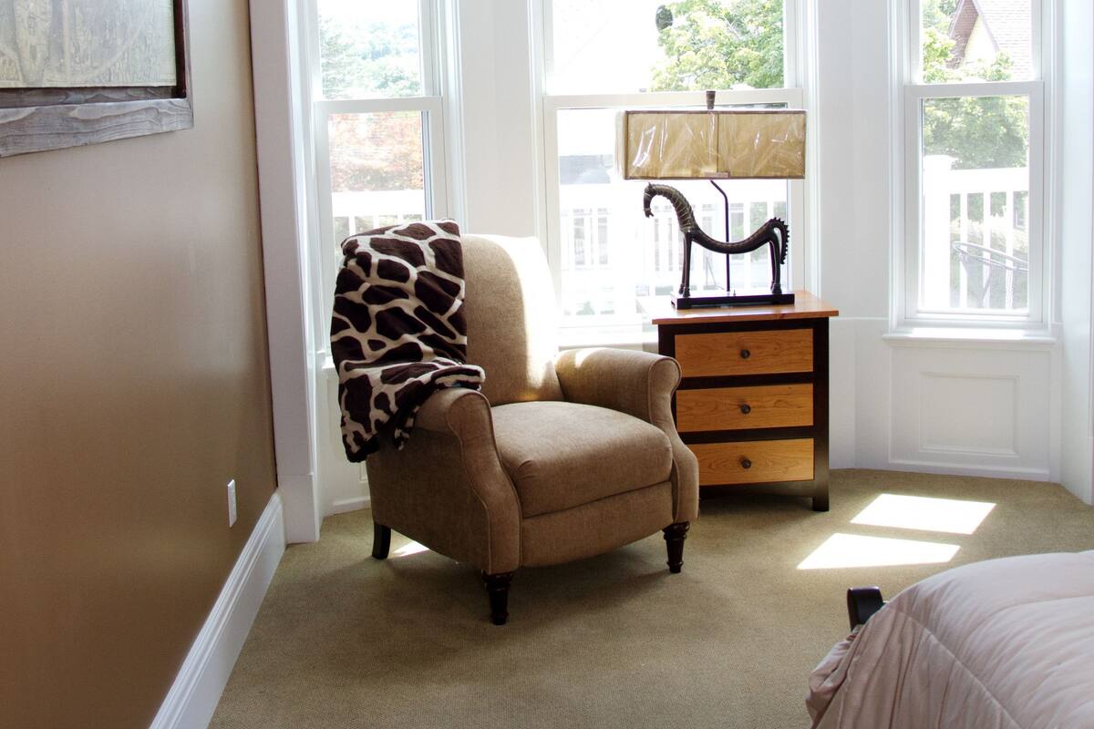 A bedroom with a large window, a chair, a nightstand, and a bed.