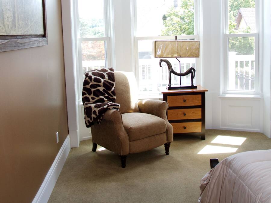 Une chambre avec une grande fenêtre, une chaise, une table de chevet et un lit.