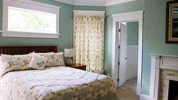 Um quarto com uma cama, mesa de cabeceira, janela, porta e lareira.