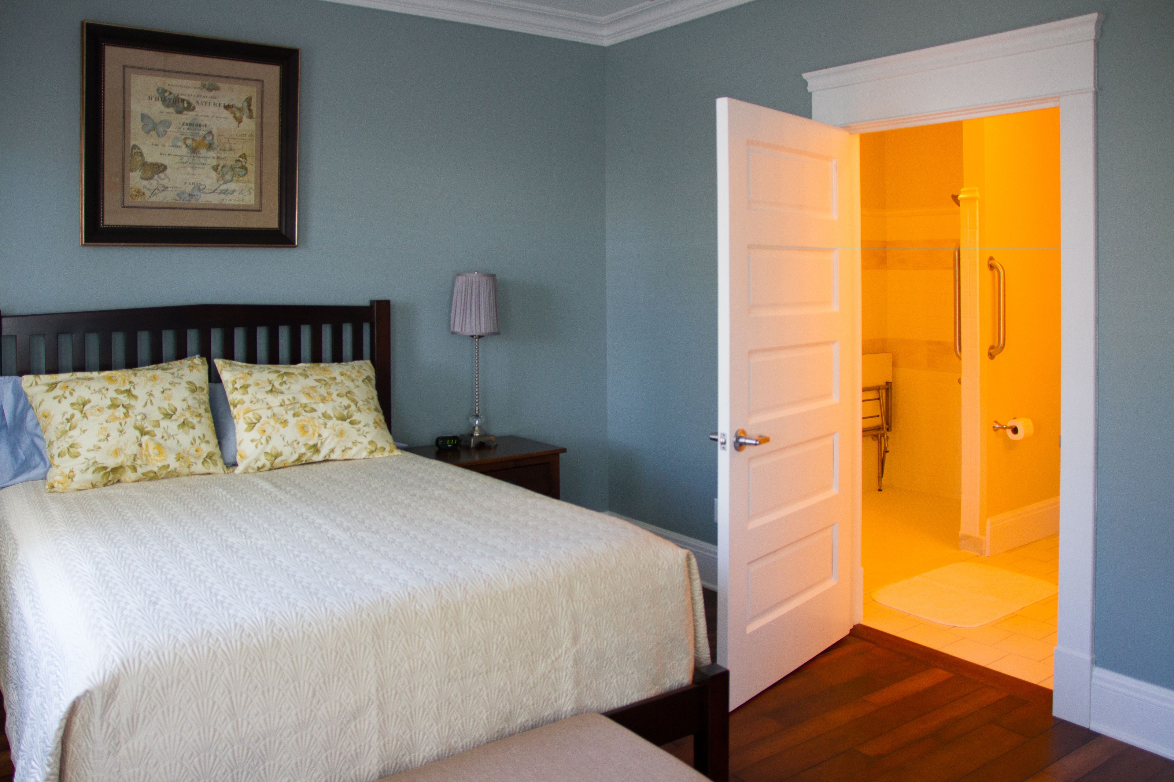 A bedroom with a bed, a nightstand, a lamp, and a door leading to a bathroom.