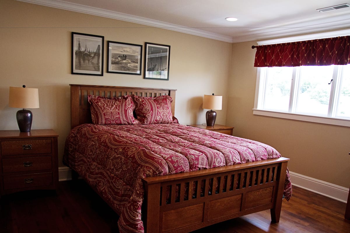 A bedroom with a large bed, two bedside tables, and a window with a red valance.