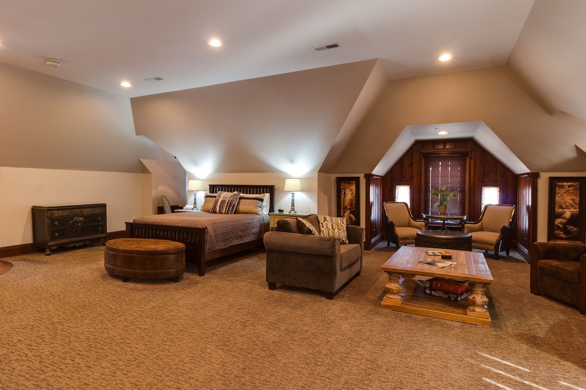 A spacious loft bedroom with a large bed, a sofa, a coffee table, and a fireplace.