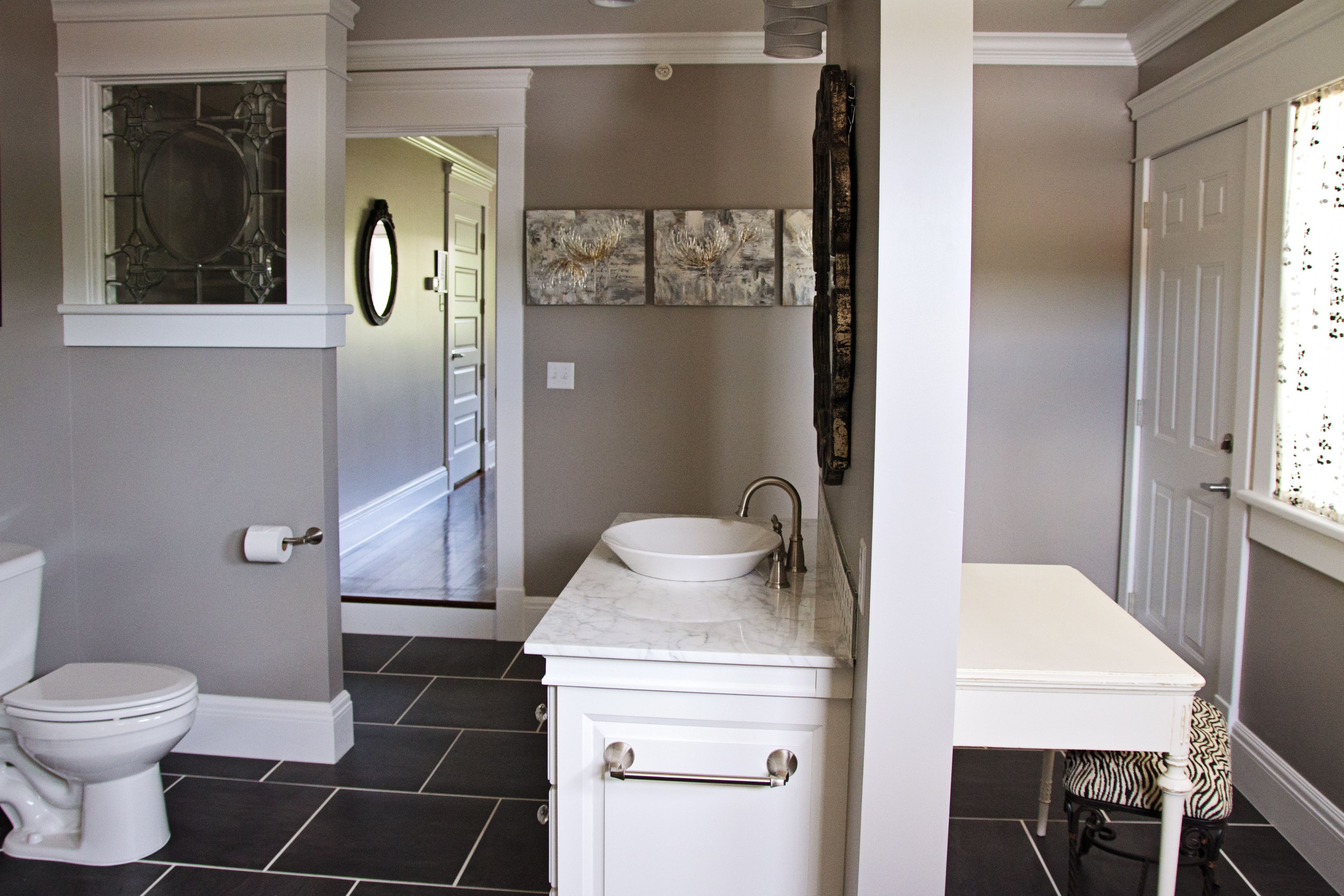 A bathroom with a white sink, toilet, and vanity. There are three framed artworks on the wall and a mirror above the sink.