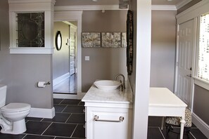 A bathroom with a white sink, toilet, and vanity. There are three framed artworks on the wall and a mirror above the sink. - Wishmaker House B&B (Bellville)