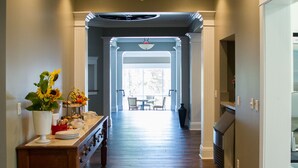 A hallway with wooden flooring, a central table with a vase of flowers, and a view into a dining area. - Wishmaker House B&B (Bellville)
