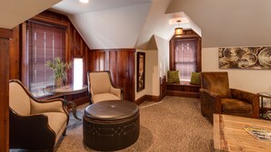 A spacious loft with a high ceiling, wooden walls, and large windows. There are two leather armchairs, a wooden coffee table, and a small side table with a lamp. - Wishmaker House B&B (Bellville)