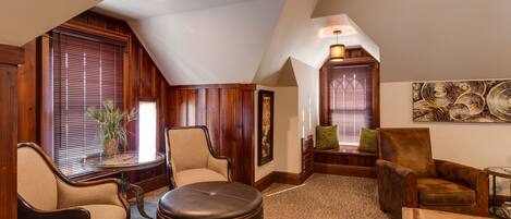 A spacious loft with a high ceiling, wooden walls, and large windows. There are two leather armchairs, a wooden coffee table, and a small side table with a lamp.