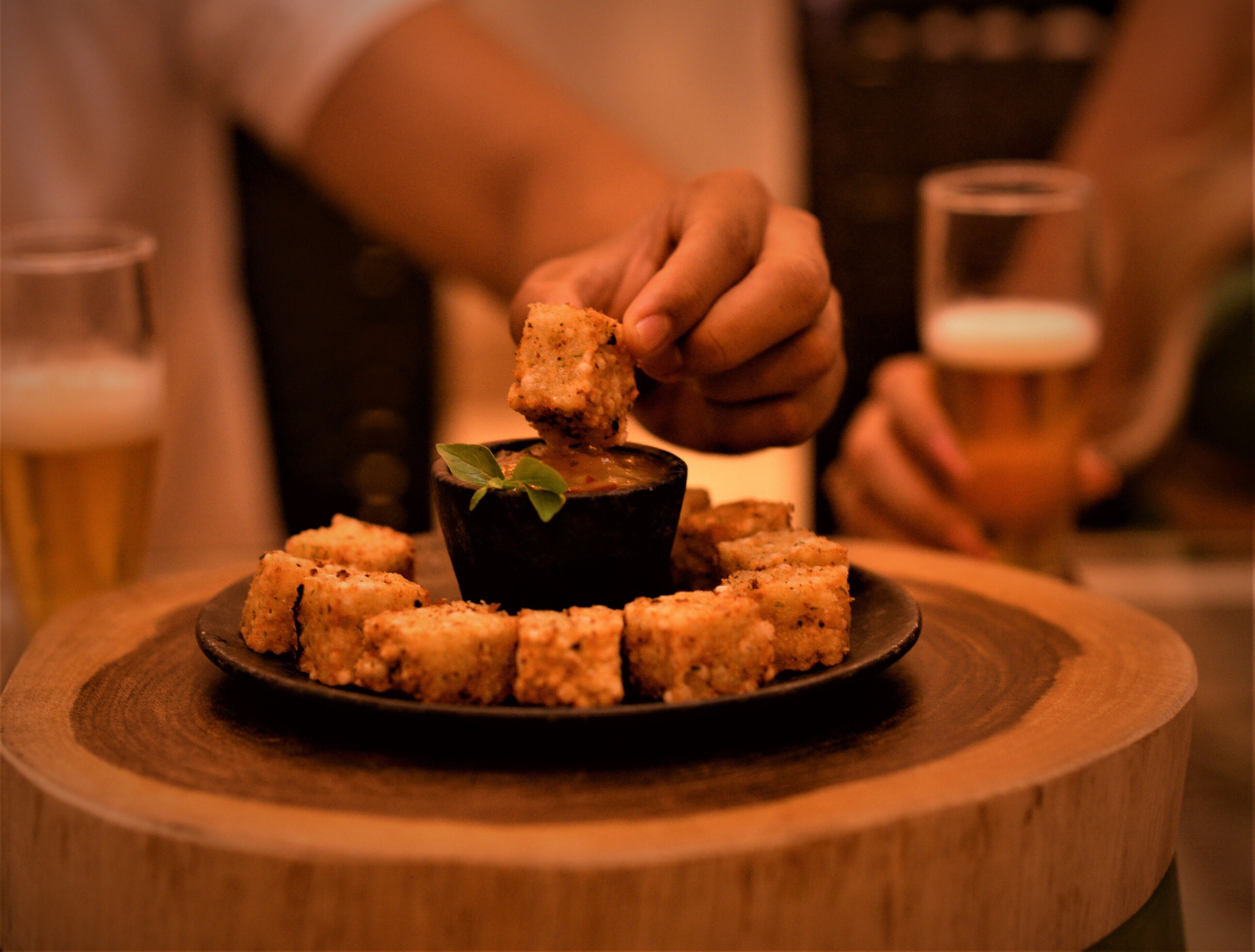 A wooden table with a black bowl containing a dipping sauce surrounded by bread cubes.
