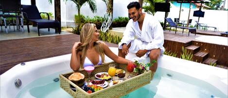 Una pareja relajándose en un jacuzzi con una bandeja de comida y bebidas.
