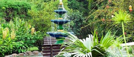 A tiered fountain in a lush garden with a wooden bench nearby.