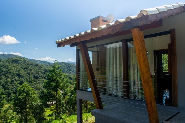 Un edificio moderno con amplios ventanales, un balcón y vistas a un paisaje verde exuberante.