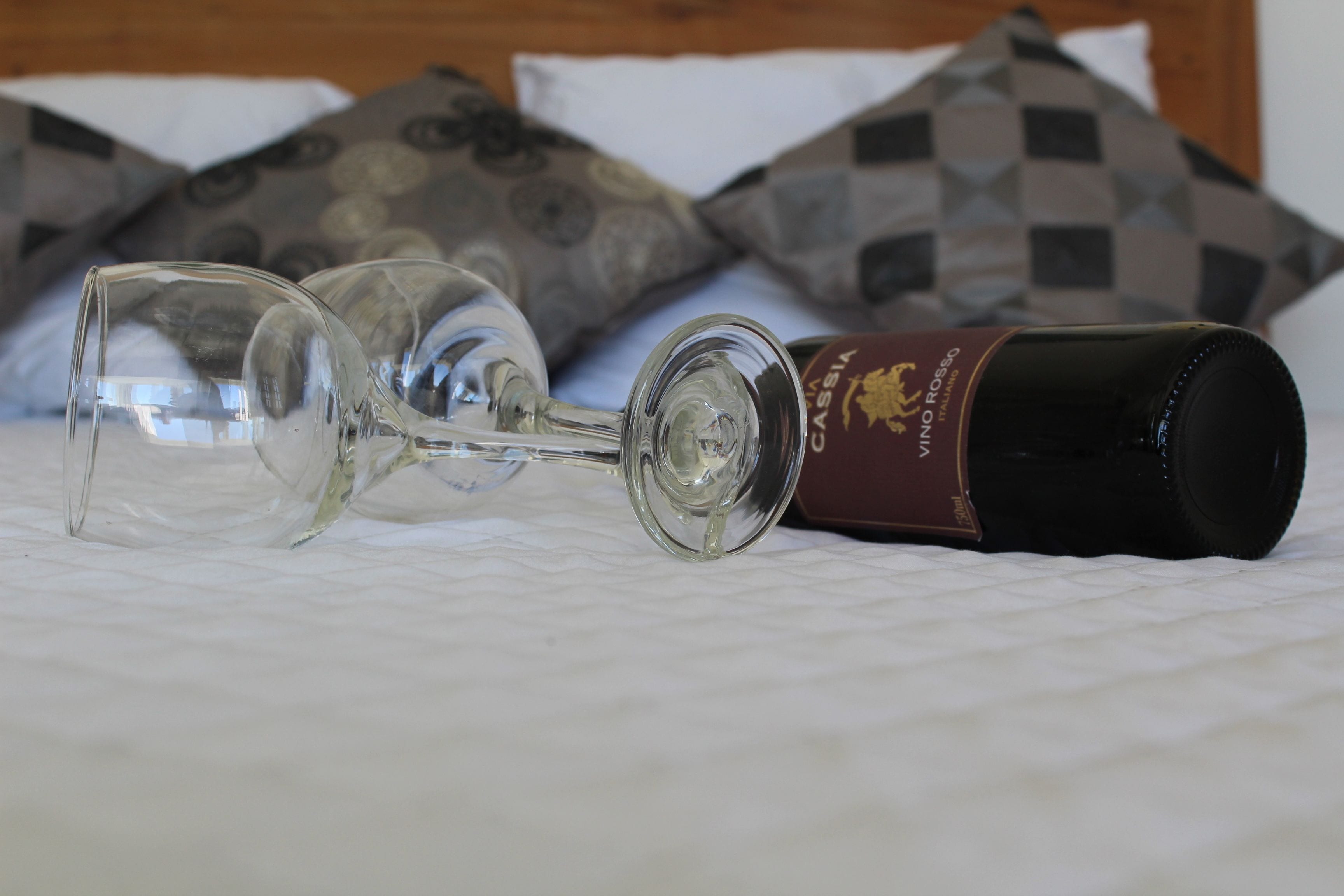 A wine glass and bottle on a bed with patterned pillows.