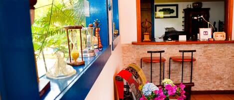 Un vestíbulo de hotel con una pared azul, una ventana con plantas, un mostrador de recepción y una silla con un florero.