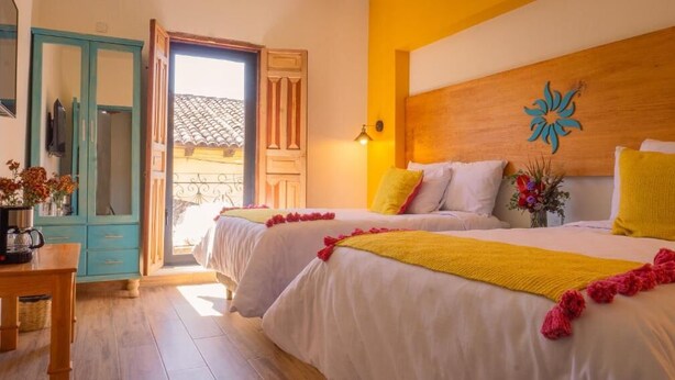 A hotel room with two beds, a wooden headboard, a decorative wall piece, and a view of the outside. - Hotel Casa del Sol (San Cristóbal de las Casas)