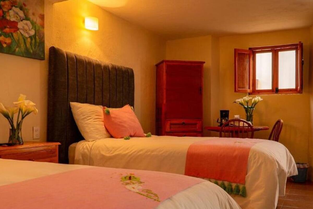 Une chambre d’hôtel avec deux lits, une table à manger, un buffet rouge et une fenêtre avec des rideaux.