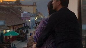 A couple embracing on a balcony overlooking a street with buildings and a sunset. - Hotel Casa del Sol (San Cristóbal de las Casas)
