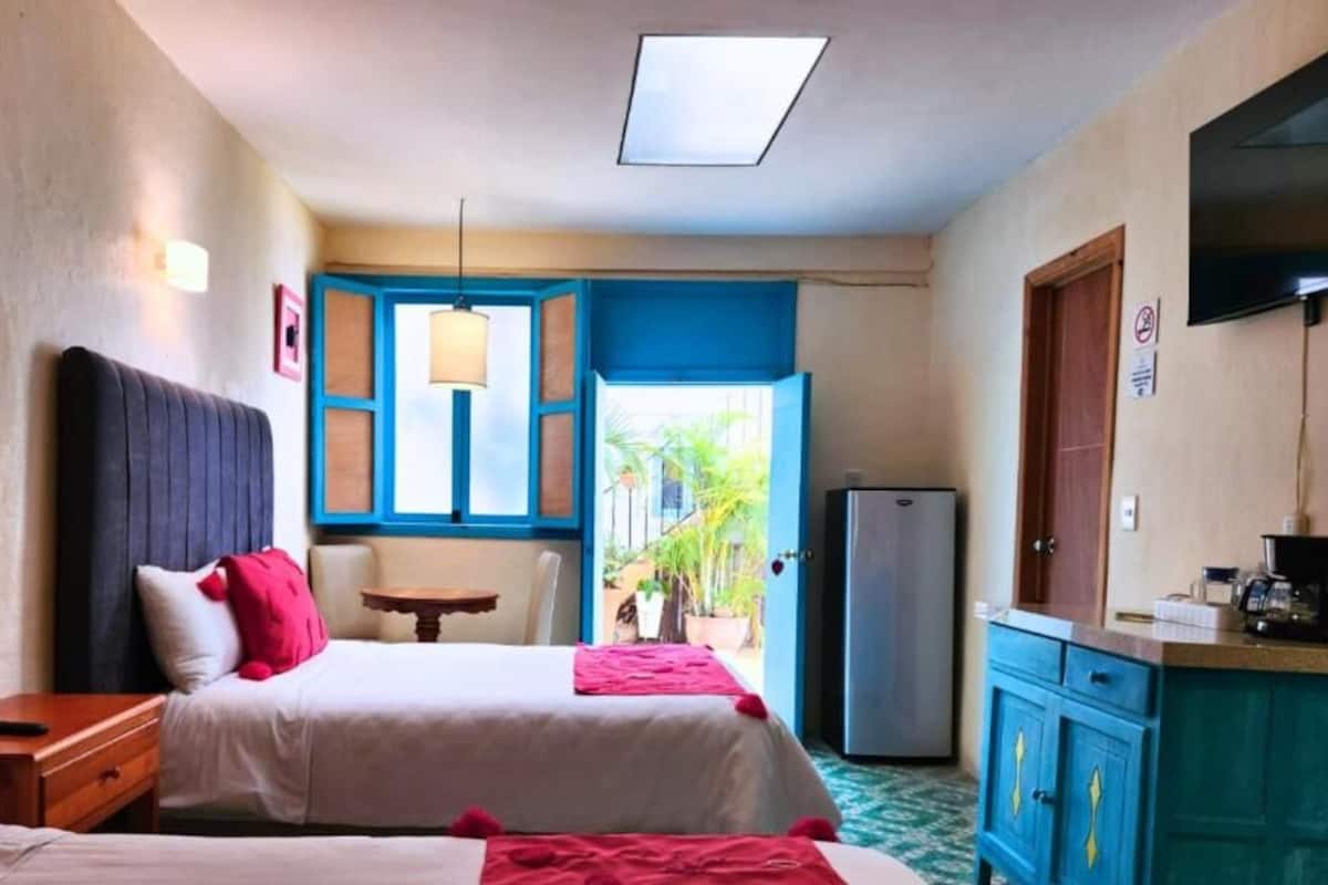 Une chambre d’hôtel avec deux lits, une petite table, un réfrigérateur et une télévision.