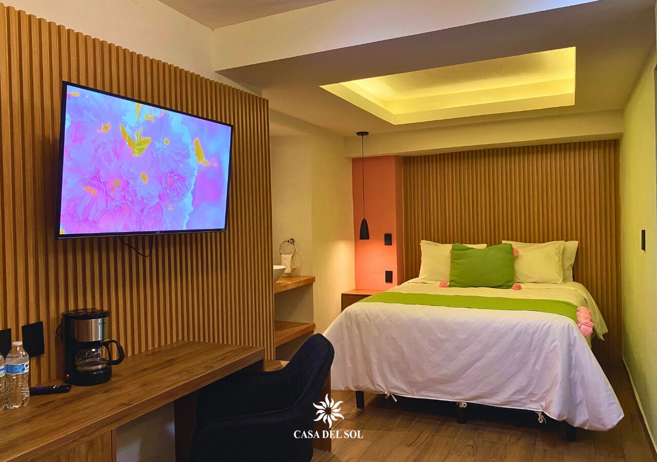 A hotel room with a bed, a desk with a coffee maker, a TV, and a wooden wall panel.
