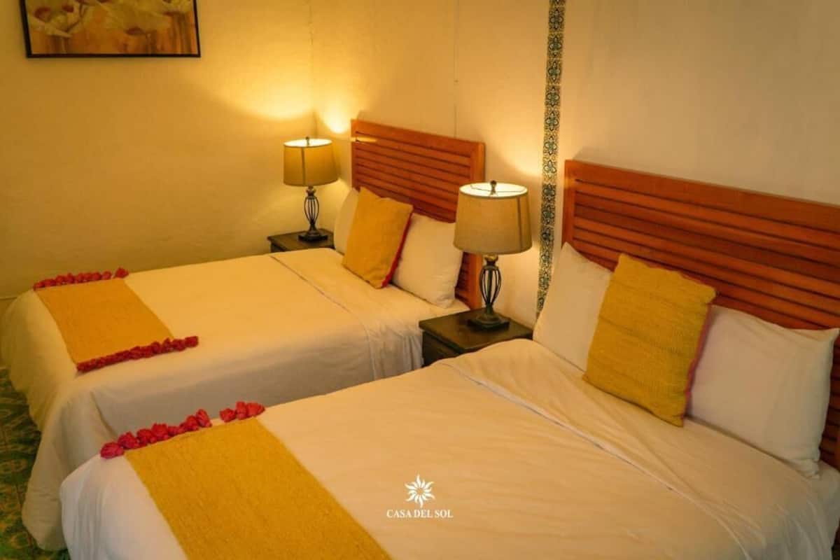 Une chambre d’hôtel avec deux lits, chacun doté d’une tête de lit en bois, de draps blancs et d’un plaid jaune. Il y a deux lampes de chevet et une petite table entre les lits.