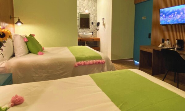 Une chambre d’hôtel avec deux lits, une salle de bain avec un lavabo et un miroir, un téléviseur fixé au mur et un bureau avec une chaise.