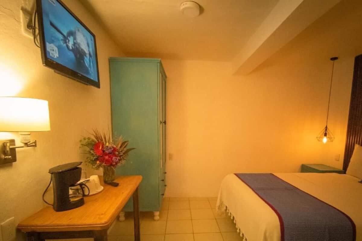 Une chambre d’hôtel comprenant un lit, un bureau avec une machine à café, un téléviseur fixé au mur, une armoire et une lampe.